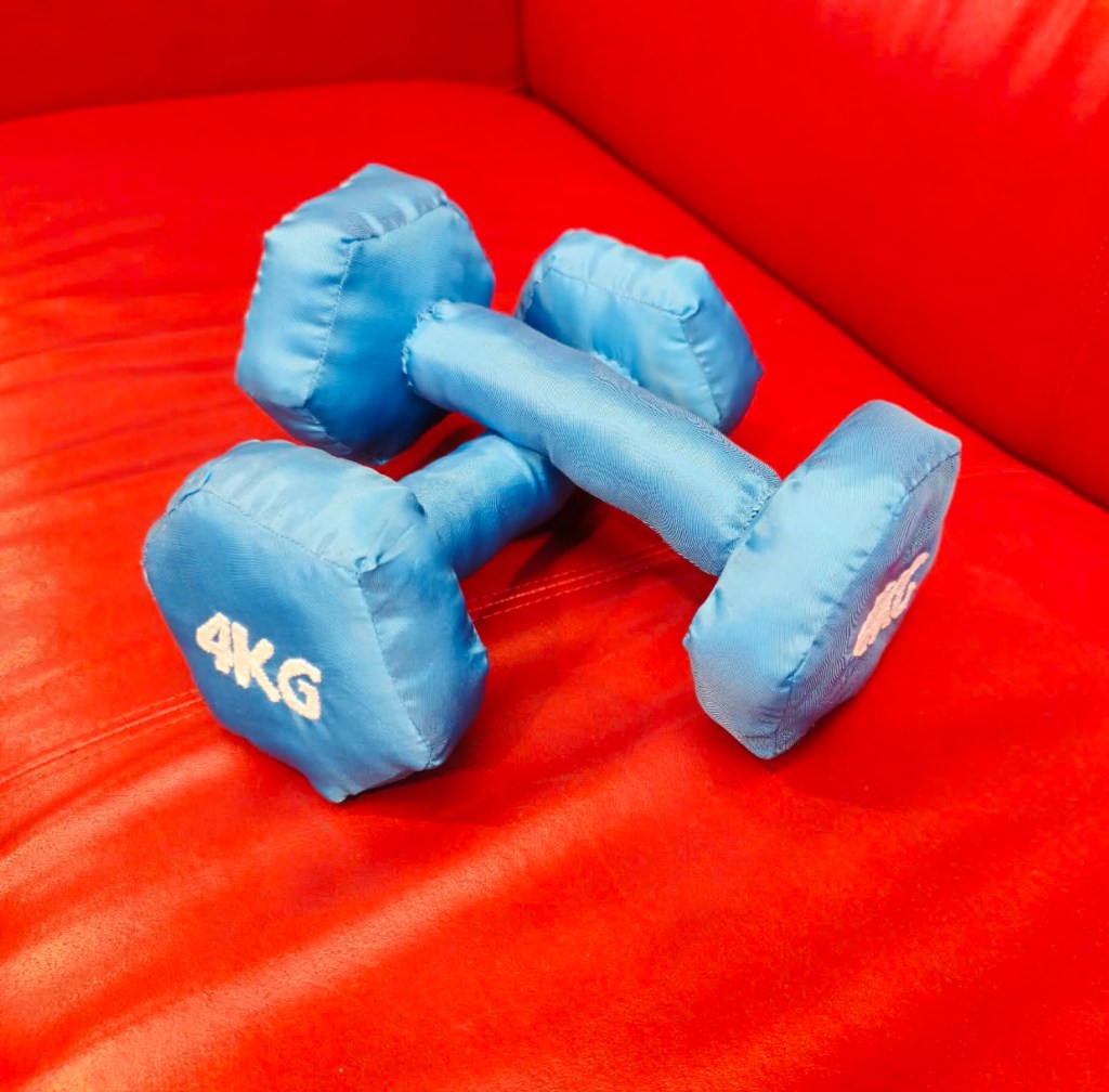 This is a photograph of Moa-Matilda Nilsson's textile sculptures, entitled 'Hantlar'. The object consists of two textile dumbbells in the colour blue, crossing each other.